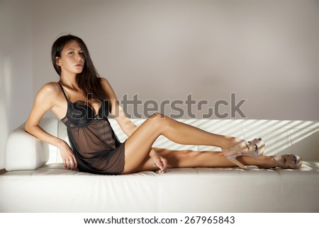 Portrait of a beautiful attractive sensuality and sexy young adult pretty brunette woman in morning sunlight wearing black nightdress lingerie in white sofa on luxury style apartment