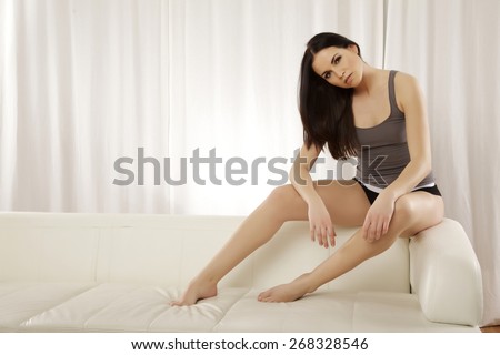 Portrait of a beautiful sensuality and attractive sexy young adult pretty female brunette woman posing in grey shirt on the white couch sofa