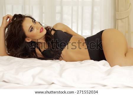 Portrait of a beautiful attractive sensuality and sexy young adult pretty brunette woman wearing black lingerie on the bed in bedroom luxury style hotel apartment
