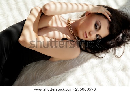 Portrait of a beautiful sensuality and attractive sexy young adult female pretty brunette woman posing in black dress on white fur