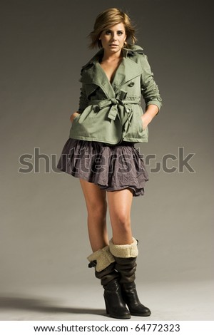 beautiful blonde girl wearing green coat and mini skirt on grey background