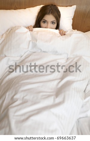 Above view of sleeping beautyful smiling brunet girl under white satin sheet