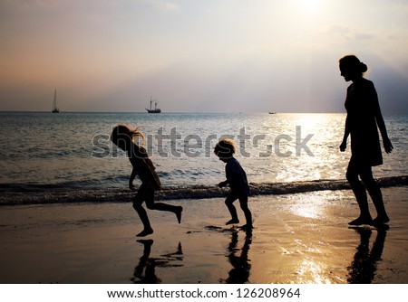Mother and two kids silhouettes running on beach at sunset