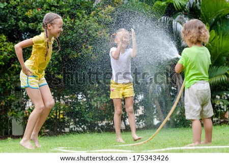 little boy is pouring a water from a hose at his sisters