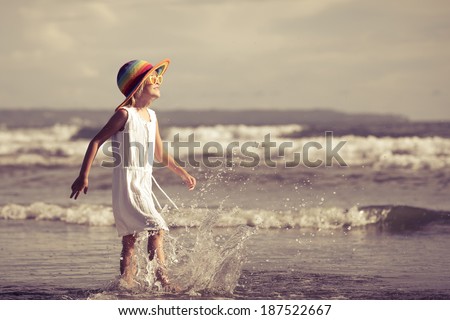 Happy little girl in the hat walking at the beach in the day time