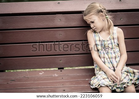 sad little girl sitting on bench in the park at the day time