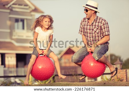 Dad and daughter jumping on inflatable balls on the lawn in front of house at the day time