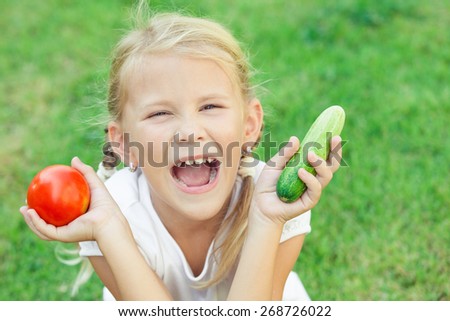 Happy little girl sitting on the grass with a  vegetables at the day time. Concept of healthy food.