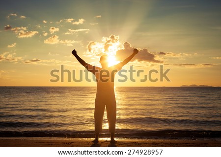 Man with his hands up at the sunset time on the beach