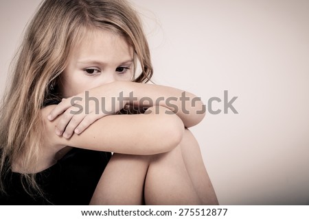 Portrait of sad blond little girl sitting near white wall