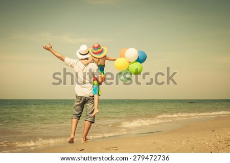 Father and daughter with balloons playing on the beach at the day time. Concept of friendly family.
