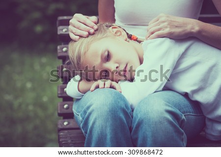 Sad mother and daughter sitting on bench in the park at the day time.