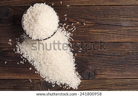 Rice in black bowl and scattered near on dark wooden table, top view