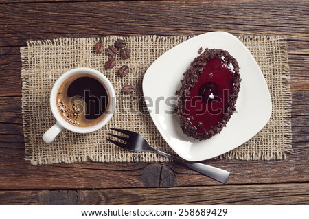Coffee cup and tasty chocolate cake with cherry jelly on dark wooden table, top view