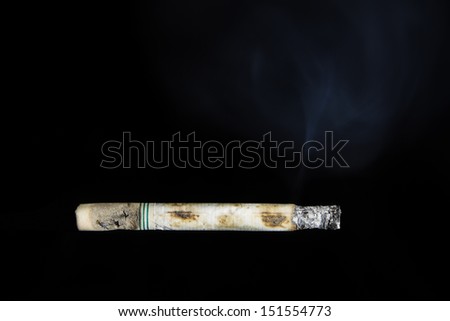 Cigarette is burned and smoke drifting out on black background.