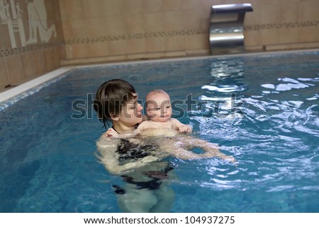 Mother is holding her child in an indoor swimming pool