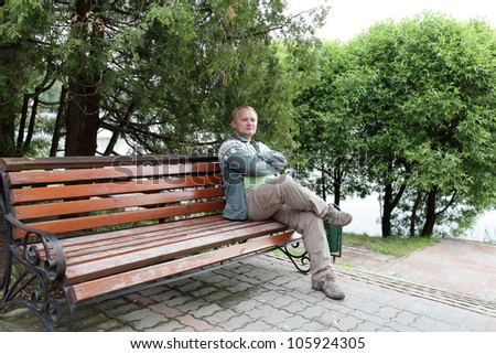 Man is resting on a wooden bench in a park