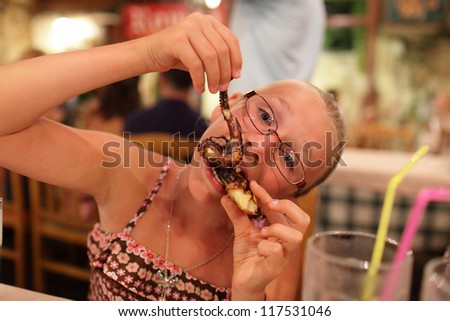 Girl is eating grilled octopus in a seafood restaurant