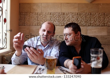 Two men are using mobile phones in a pub