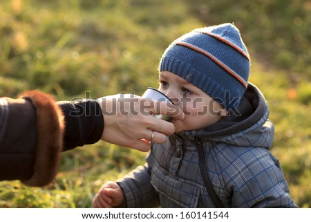 Child drinks tea in the autumn park