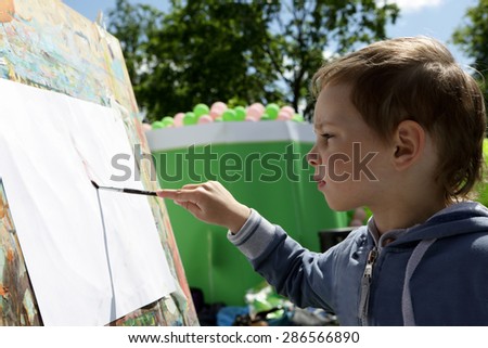 Child draws paints on the paper in the park