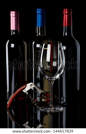 Three wine bottles, a wineglass and corkscrew on a black reflective background