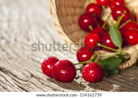 Some ripe Cherries with sparkling Water Drops in small Basket on a old Wooden Table