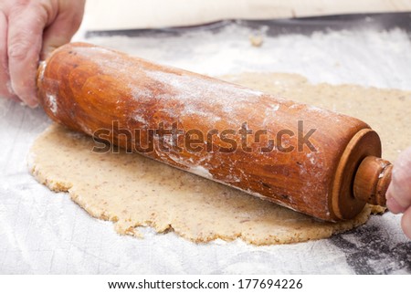 Hands holding a rolling pin to roll out which a cookie dough