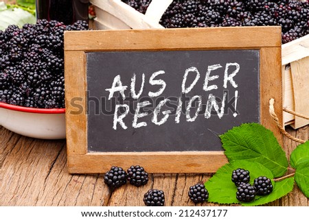 Slate blackboard with the Germans words: Aus der Region (From the region), in front of ripe blackberries on a rustic wooden table