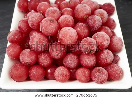 Top view of frozen currants covered with ice crystals in a white porcelain bowl on a slate platter