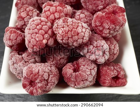 Macro shot of some frozen raspberries in a white porcelain dish on a slate platter