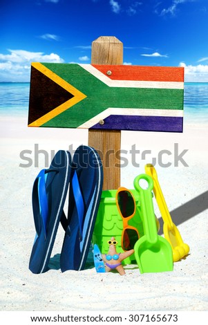 Wooden signboard with the south africa flag, blue flip flops and colorful beach toys on the sunny beach