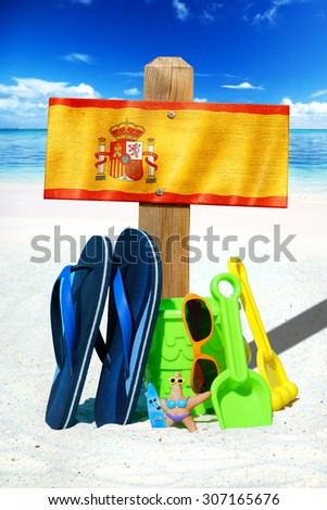 Wooden signboard with the spain flag, blue flip flops and colorful beach toys on the sunny beach