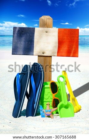 Wooden signboard with the france flag, blue flip flops and colorful beach toys on the sunny beach