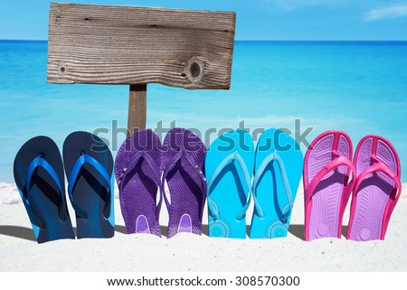 Wooden signboard with copy space behind a row of colorful flip flops on the sunny beach