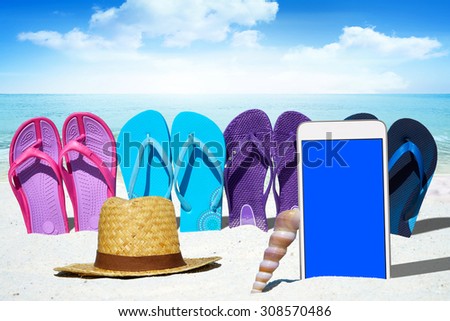 White smart phone with blank screen display, flip flops and  a straw hat on the sunny beach