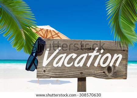 Wooden signboard with text message VACATION and a sunglasses under palm fronds on the summer beach