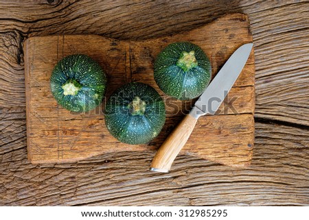 Three round and ripe Zucchinis and a kitchen knife on rustic wooden cutting board