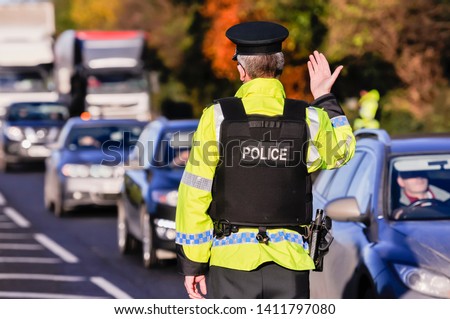 Belfast, Northern Ireland. 24 Nov 2016 - An armed PSNI officer waves on traffic during a vehicle checkpoint.