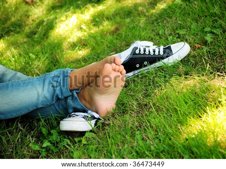 feet of the girl teenager and gym shoes on a green grass of a lawn in park