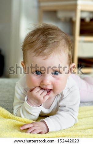 Cute caucasian baby with beautiful eyes lying on stomach and looking around.