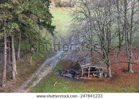 Old wooden shelter under deciduous trees and path in winter nature. Outdoors theme.