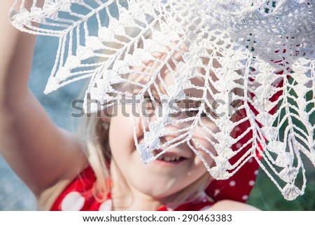 Little caucasian girl is laughing and hiding behind the crochet hat. Beauty and fashion.
