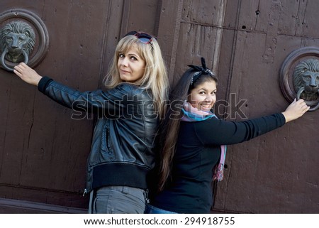 Two women knocking on an old wooden door with knockers.