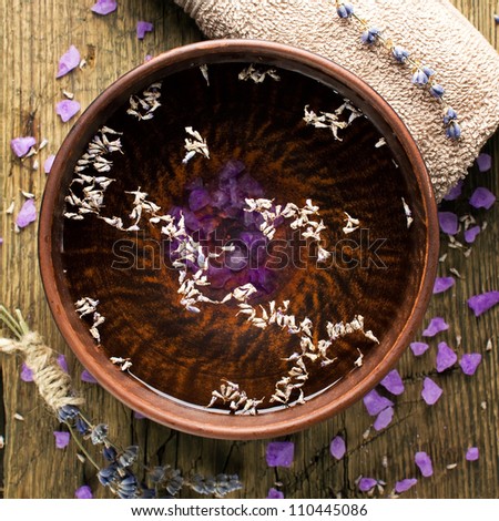 Bowl of pure water and lavender petals on the old wooden surface. Spa treatments composition