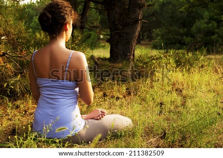 girl sitting in the lotus position on the grass in the forest