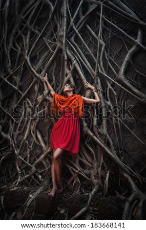 young slender girl in roots of a tree of a huge tree