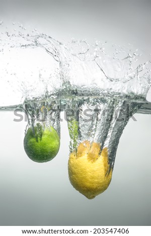 Lime and lemon falling into the water with splash and little air bubbles