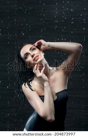 Half-length portrait of sexy brunette standing in great black swimsuit under the rain and dreaming about her future vocation