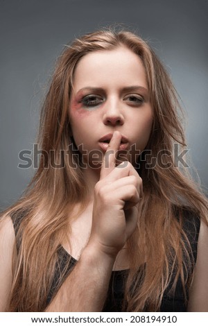 Half-length portrait of scared fair-haired young girl with the black eye wanted but cannot tell us the truth. Isolated on grey background